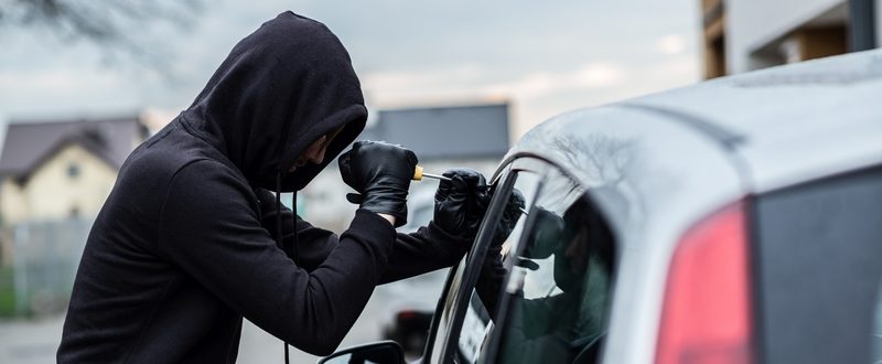 Car thief trying to break into a car with a screwdriver. Car thief